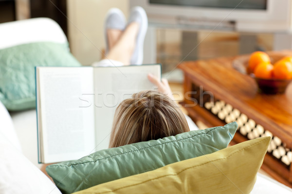 Stock photo: Woman reading a book lying on a sofa