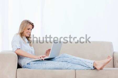 A young woman is lying on a couch and typing on her laptop Stock photo © wavebreak_media
