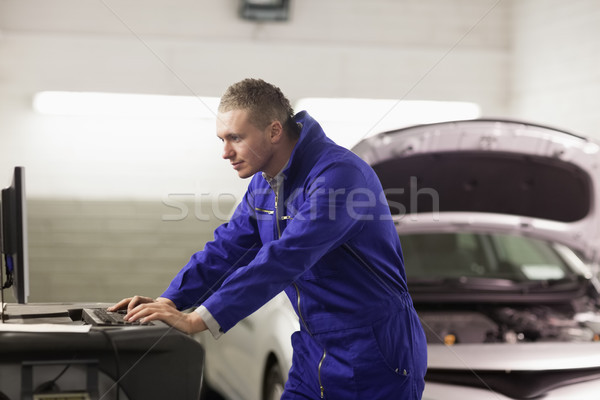 Stock photo: Mechanic looking at a computer in a garage