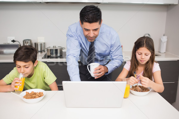 Father using laptop and kids having breakfast in kitchen Stock photo © wavebreak_media