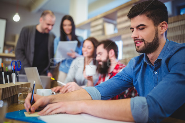 Businessman writing on paper while coworkers in background Stock photo © wavebreak_media