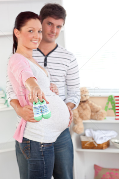 Cheerful pregnant woman holding baby shoes while husband touching her belly in the room of their fut Stock photo © wavebreak_media