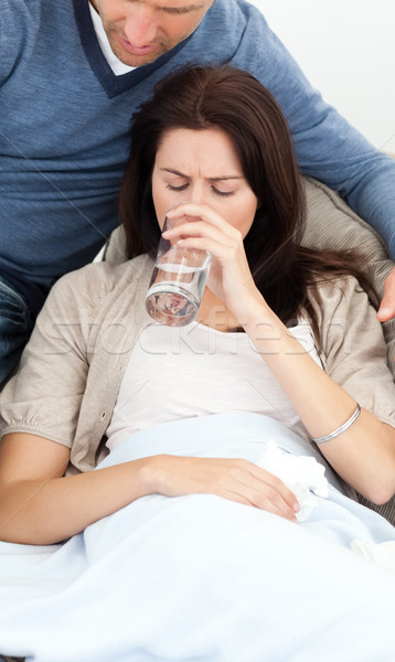 Sick woman drinking water lying on the sofa with her boyfriend Stock photo © wavebreak_media
