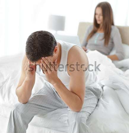 Stressed man sitting on his bed while his girlfriend working on the laptop on the background Stock photo © wavebreak_media