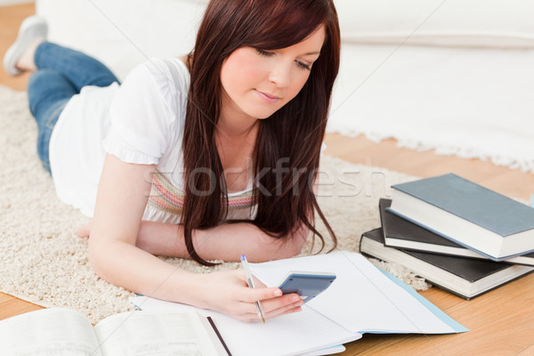 Good looking red-haired female studying for while lying on a carpet in the living room Stock photo © wavebreak_media