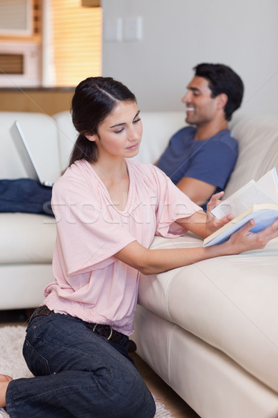 Stock photo: Portrait of a woman reading a book while her fiance is using a laptop in their living room