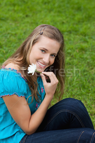 Smiling young girl holding a flower next to her face while sitting in a park Stock photo © wavebreak_media