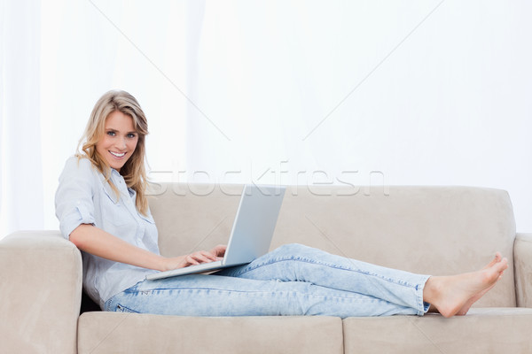 A Smiling Woman Lying Down On A Couch Has A Laptop On Her Legs