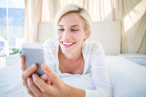 Smiling blonde woman lying on the bed and texting with her mobil Stock photo © wavebreak_media