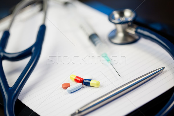 Note pad with stethoscope and pen along with  serynge and capsules on a blue and dark background Stock photo © wavebreak_media