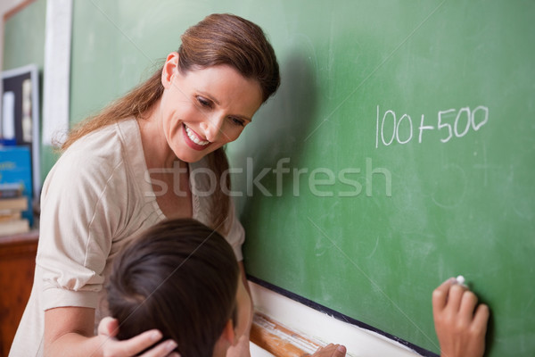 Stock photo: Smiling schoolteacher helping a schoolboy doing an addition on a blackboard