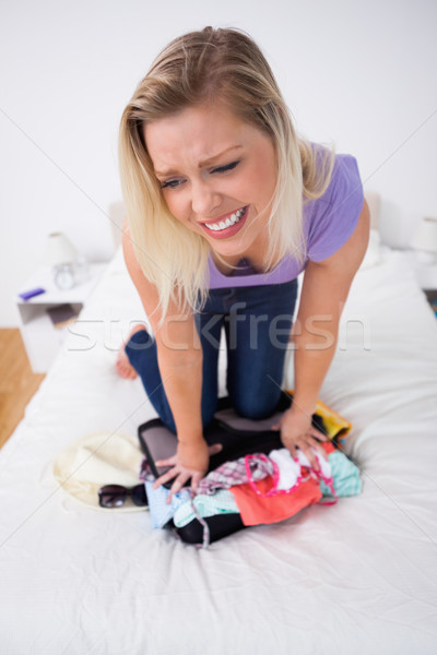 Blonde trying to close her suitcase on her bed Stock photo © wavebreak_media