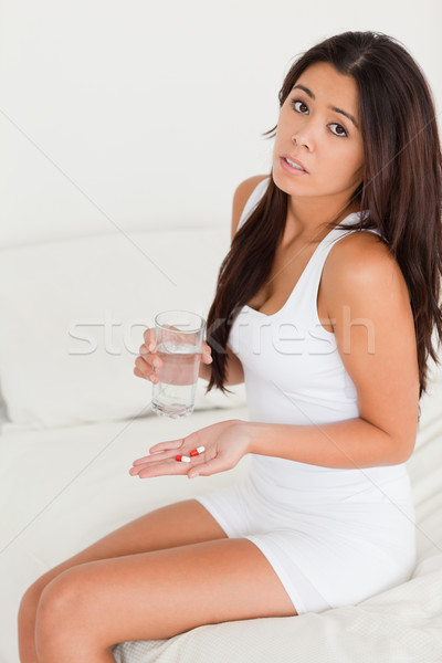 dark-haired woman having stomach ache taking pills looking into camera in bedroom Stock photo © wavebreak_media