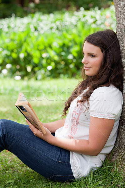 Young thoughtful girl sitting against a tree while reading a book in a public garden Stock photo © wavebreak_media