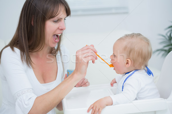 Stock photo: Mother feeding a baby while opening her mouth in living room