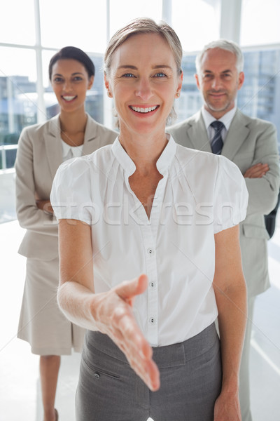 Smiling businesswoman giving a handshake with colleagues behind Stock photo © wavebreak_media
