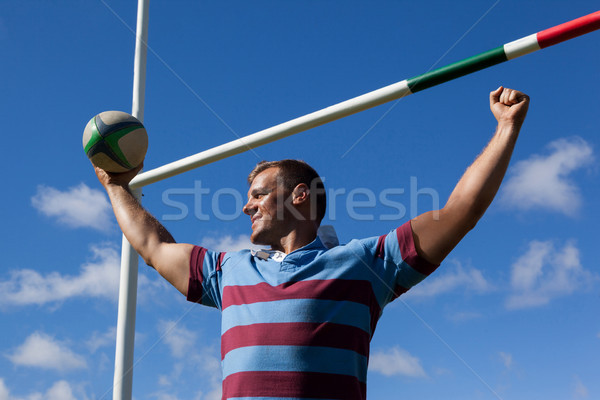 Smiling rugby player holding ball with arms raised against blue sky Stock photo © wavebreak_media
