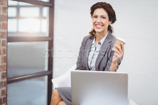 Businesswoman holding disposable cup sitting on desk Stock photo © wavebreak_media