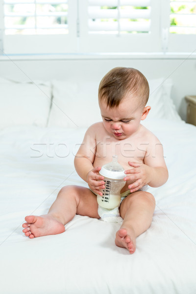 Baby boy sitting with milk bottle on bed at home Stock photo © wavebreak_media