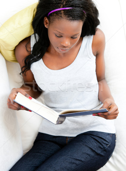 Concentrated young woman reading a book sitting on a sofa at home Stock photo © wavebreak_media