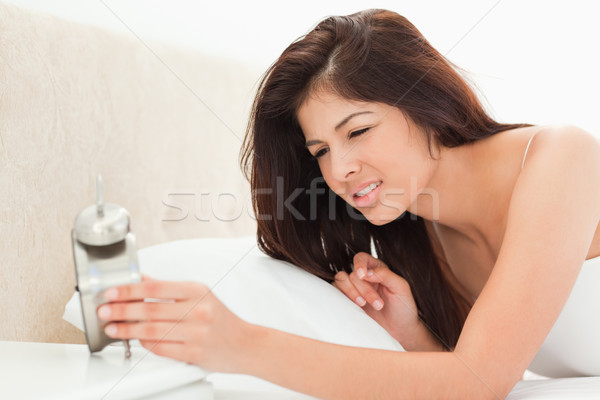 Stock photo: A woman has awoken and checked her clock. She is tired as her eyes look heavy.