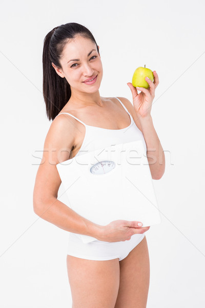 Stock photo: Smiling brunette holding weighing scales and apple
