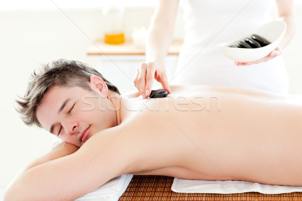 Charming young man receiving a massage with hot stone in a spa center Stock photo © wavebreak_media