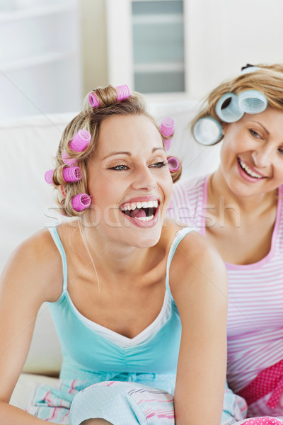 Stock photo: Laughing women wearing hair rollers sitting on the sofa at home