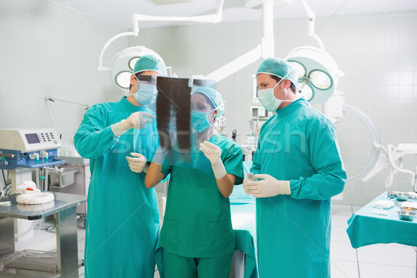 Stock photo: Surgical team talking about a X-ray in an operating theatre