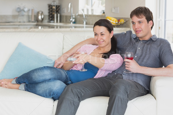 Stock photo: Young couple sitting on the couch and watching television while drinking wine