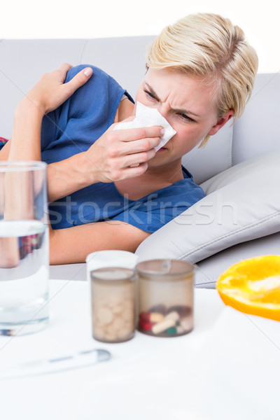 Stock photo: Sick blonde woman blowing her nose and looking at pills