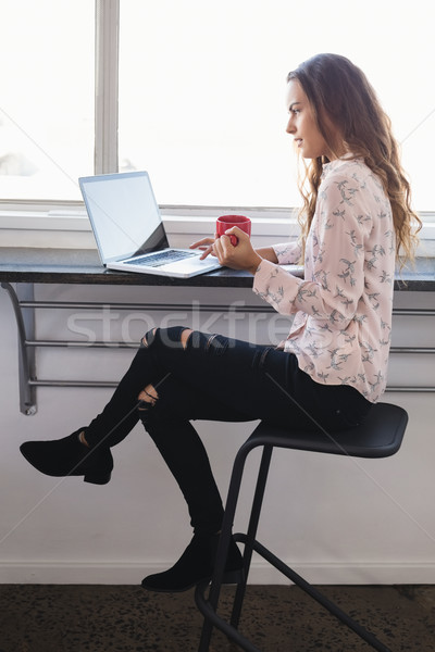 Stock photo: Businesswoman holding coffee cup while working on laptop
