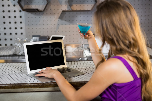 Beautiful woman using laptop while having cocktail Stock photo © wavebreak_media