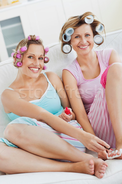 Stock photo: Cheerful female friends doing pedicure and wearing hair rollers at home