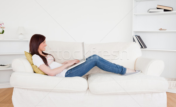 Beautiful red-haired female relaxing with her laptop while lying on a sofa in the living room Stock photo © wavebreak_media