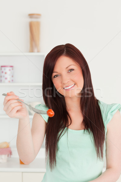 Beautiful red-haired woman cutting eating a cherry tomato in the kitchen in her appartment Stock photo © wavebreak_media