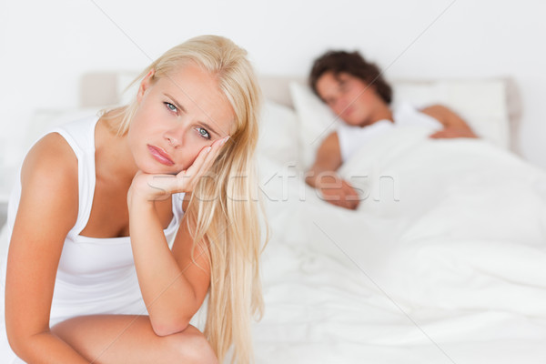 Unhappy woman sitting on a bed while her fiance is sleeping with the camera focus on the foreground Stock photo © wavebreak_media