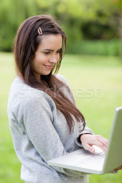 Happy young woman holding her laptop while standing upright in a parkland Stock photo © wavebreak_media