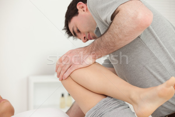 Stock photo: Woman lying while a physiotherapist folded her leg on her chest in a physio room