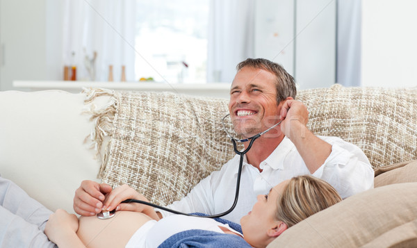Man listening his wife's belly with his stethoscope at home Stock photo © wavebreak_media
