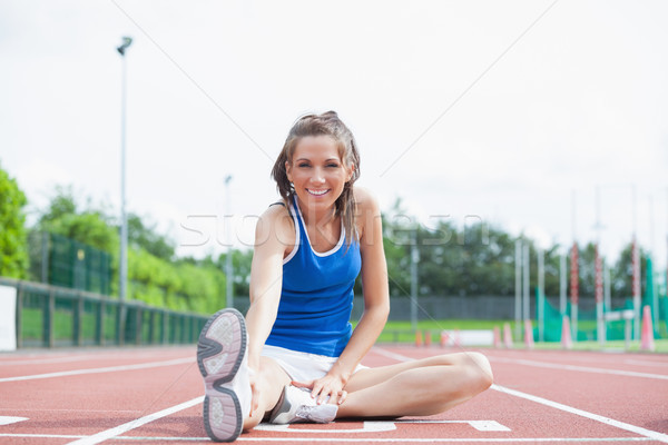 Stock photo: Cheerful woman stretching her leg on a track