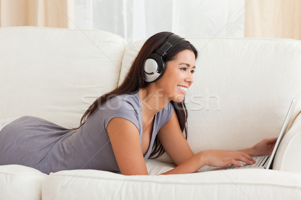 Stock photo: smiling woman with thumb up and earphones lying on sofa in livingroom