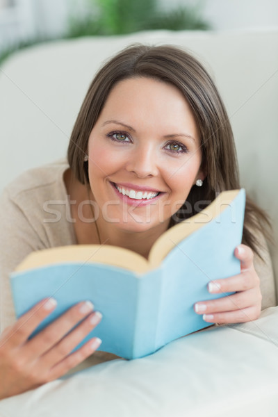 Woman lying on sofa looking happy in the living room with a book Stock photo © wavebreak_media