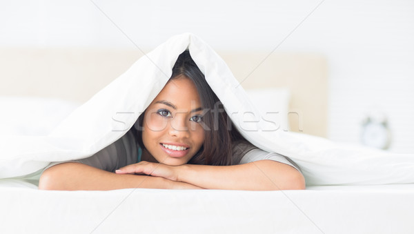 Pretty girl lying under the duvet smiling at camera Stock photo © wavebreak_media
