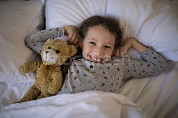 Smiling girl lying on bed with teddy bear in bedroom Stock photo © wavebreak_media