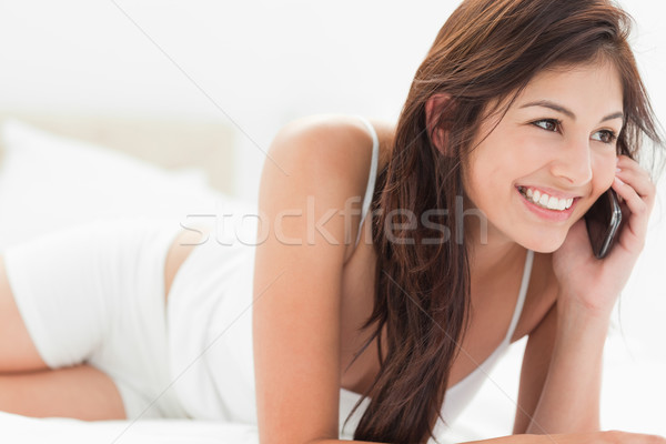 Stock photo: A woman lies forward on her bed making a call as she smiles. 