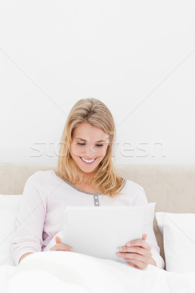 A centered shot of a woman in watching a tablet pc while sitting in bed and smiling. Stock photo © wavebreak_media