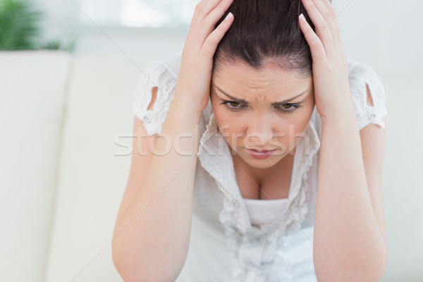 Annoyed woman sitting on the couch in the living room and holding her head in her hands Stock photo © wavebreak_media