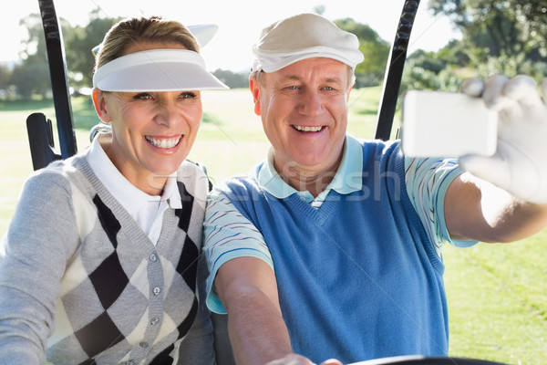Stock photo: Happy golfing couple sitting in golf buggy taking a selfie