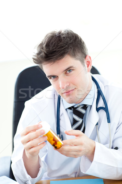 Serious male doctor holding pills sitting at his desk Stock photo © wavebreak_media